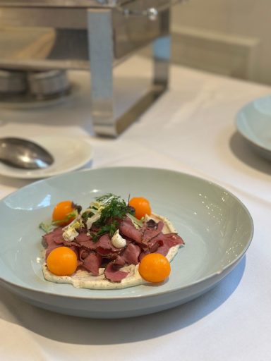 Gericht mit dünn geschnittenem Fleisch, Melonenbällchen und einer cremigen Sauce.