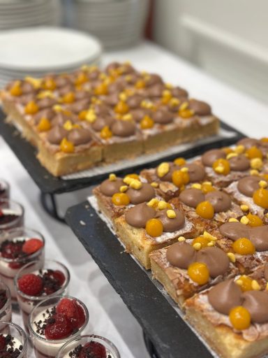 Süßer Blechkuchen mit Schokoladenglasur und goldenen Früchten, daneben kleine Dessertgläser.