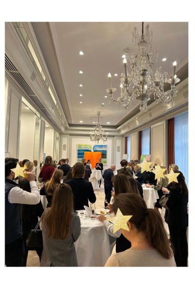 Gruppen von Menschen stehen in einem eleganten Raum mit Tischen und Kunstwerk im Hintergrund.